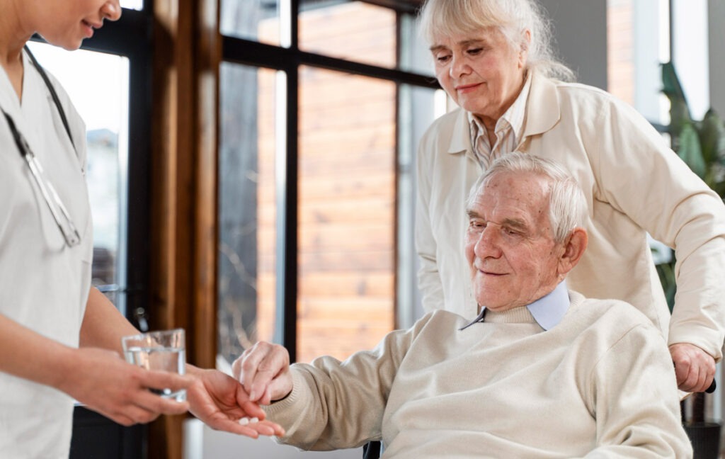 Betreuungskraft reicht Seniorin Medikamente